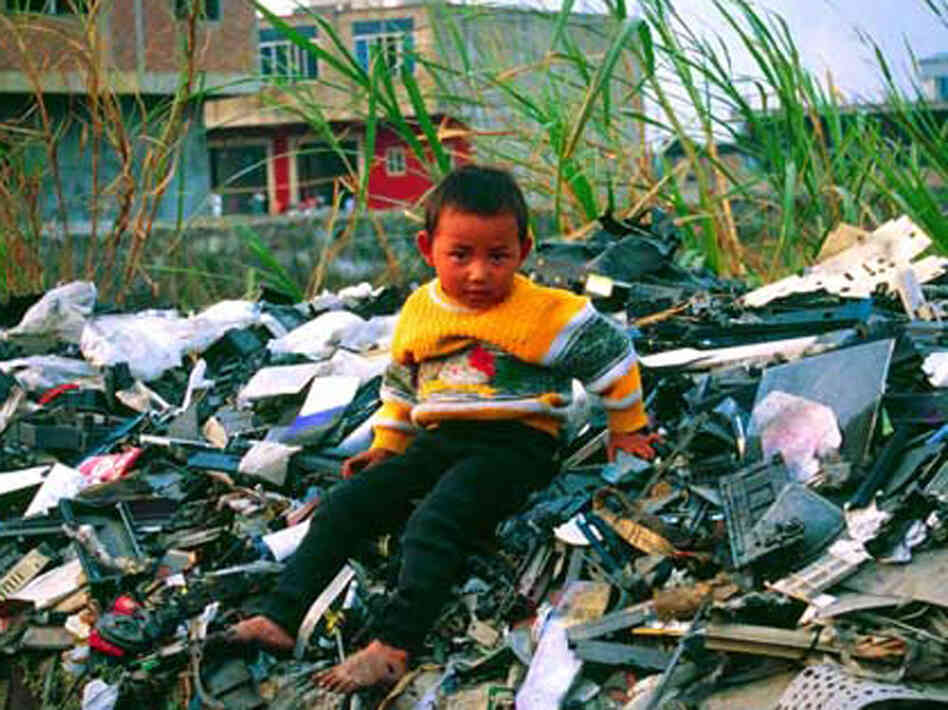 migrant child sits atop a pile of unrecyclable computer waste imported to Guiya, China, from other countries.