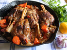 Lamb shanks and vegetables in a cast-iron pan, with parsley, lemon and garlic on a table Lamb shanks and vegetables in a cast-iron pan, with parsley, lemon and garlic on a table