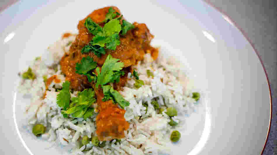 A piece of butter chicken rests on a bed of rice and peas, with a garnish of greens