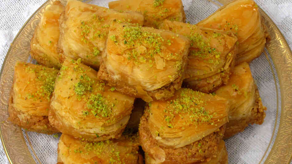 A plate full of baklava, cut into squares and dusted with ground pistachio