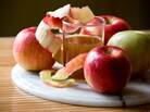 A glass of apple cider is nestled among apples of varying hues on a marble charger A glass of apple cider is nestled among apples of varying hues on a marble charger