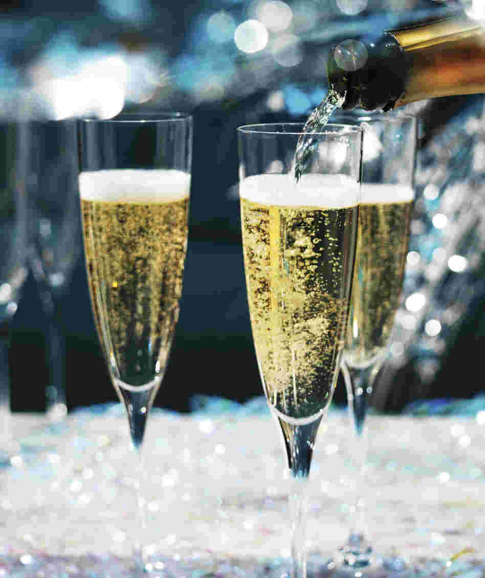 Champagne being poured into champagne flutes, in a very sparkly, festive party.