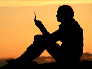 woman looks at her cellphone as the sun sets in the background.