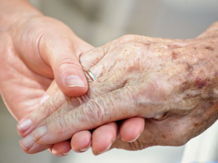 A young woman holds an elderly woman's hand.  class=
