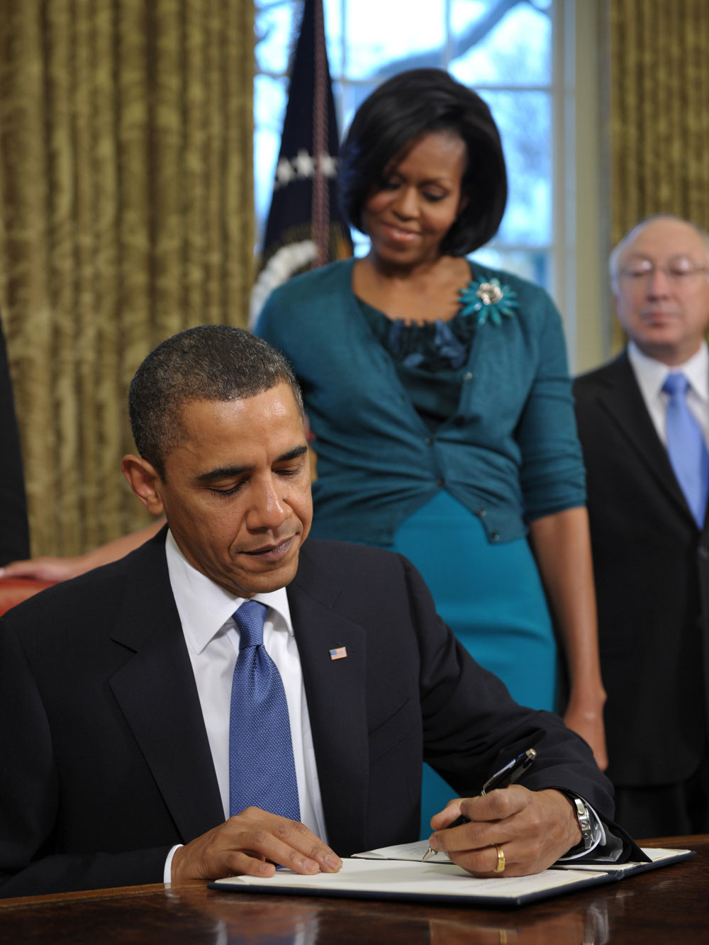 President Barack Obama signs a memorandum on childhood obesity while First Lady Michelle Obama looks on.