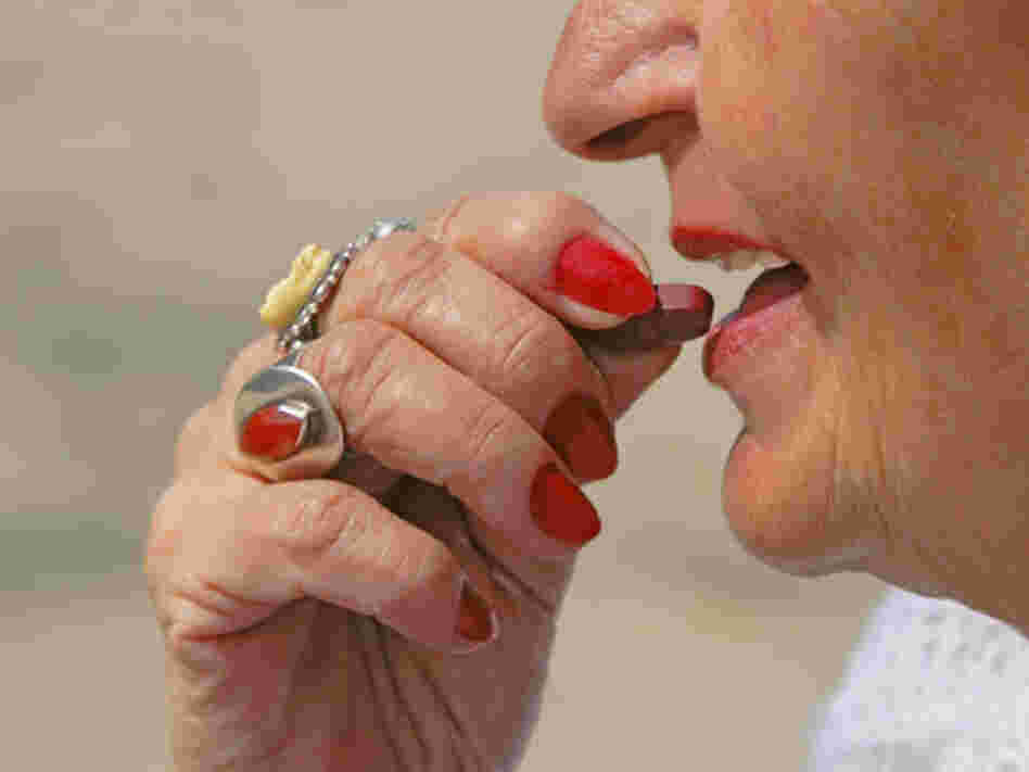 Older woman puts vitamin tablet in her mouth.