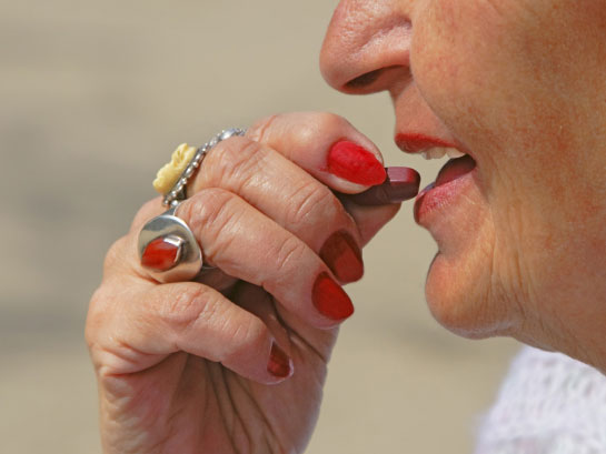 Older woman puts vitamin tablet in her mouth.