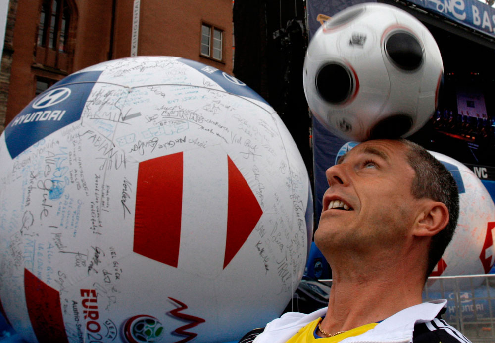 A man heads a ball as he plays next to a blown up ball bearing signatures, in the fan zone in downtown Basel, Switzerland, Friday, June 6, 2008. The Euro 2008 European Soccer Championships in Austria and Switzerland kicks off on Saturday. (AP Photo/Ivan Sekretarev)