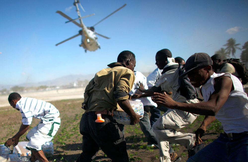 Men scramble Saturday to grab some of the relief supplies delivered by a U.S. military helicopter. (