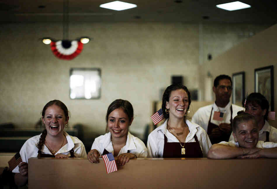 The serving staff watches from the back as Obama greets customers and workers at the Deli Den in Fort Lauderdale, Fla.
