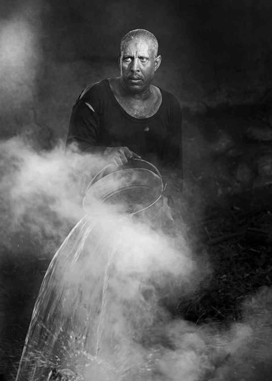 "Working man pouring water onto a fire to produce charcoal for shisha pipes near Luxor, Egypt." 