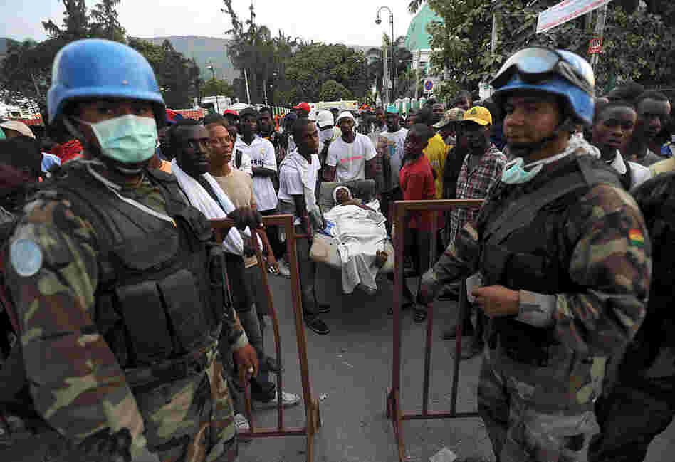 Bolivian U.N. Blue Helmet soldiers stand guard at an aid center in Port-au-Prince as a group of Haitians carries a victim. 