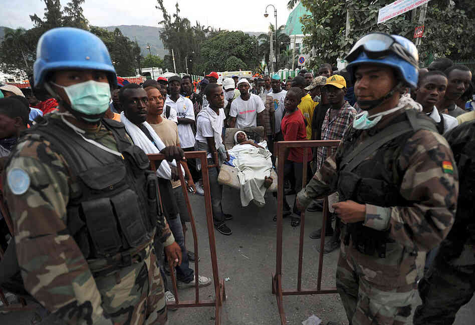 Bolivian U.N. Blue Helmet soldiers stand guard at an aid center in Port-au-Prince as a group of Haitians carries a victim. 