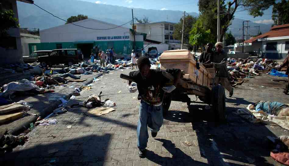 Men run with a casket after locating a family member's body among the hundreds strewn in the streets outside the National Hospital in Port-au-Prince.