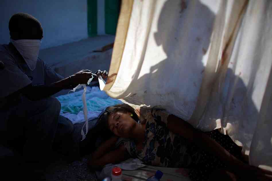 A man tries to cover his wife with any bit of shade he can find while awaiting help outside the National Hospital in Port-au-Prince.