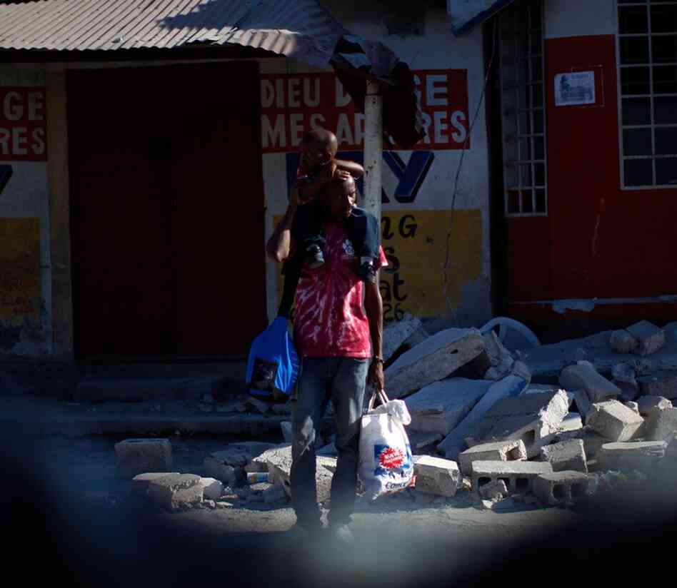 A man stands with his child on his shoulders outside a collapsed building. In what has long been the Western Hemisphere's poorest nation, shock was giving way to despair.