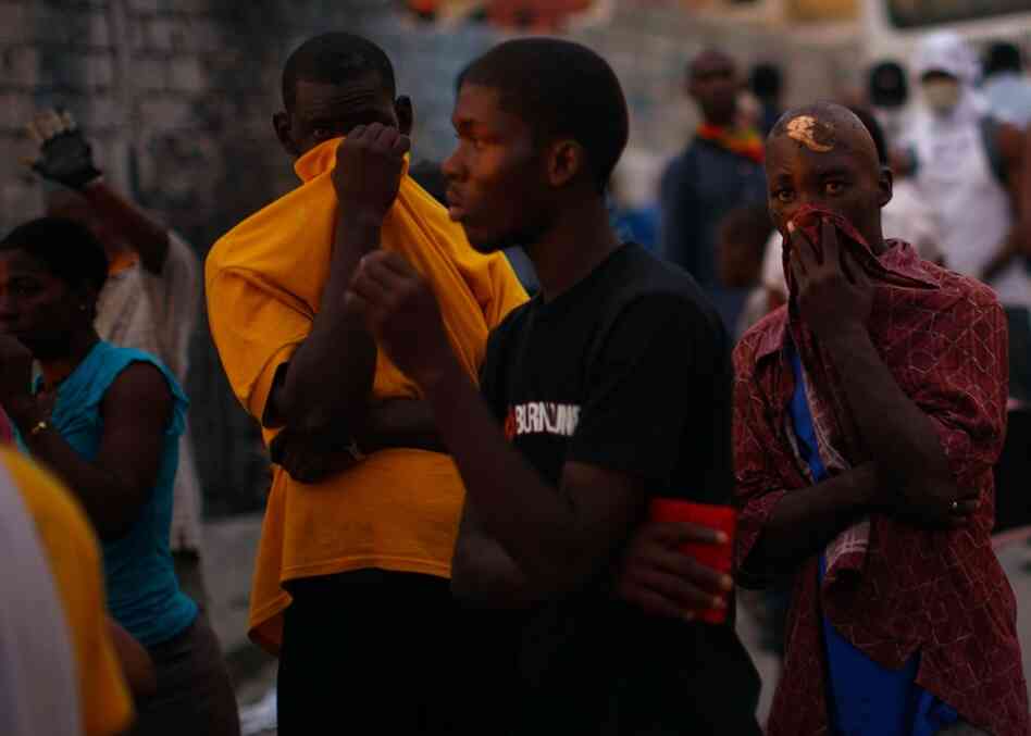 Haitian men cover their faces from the stench of decay as bodies are removed from the streets of Port-au-Prince.