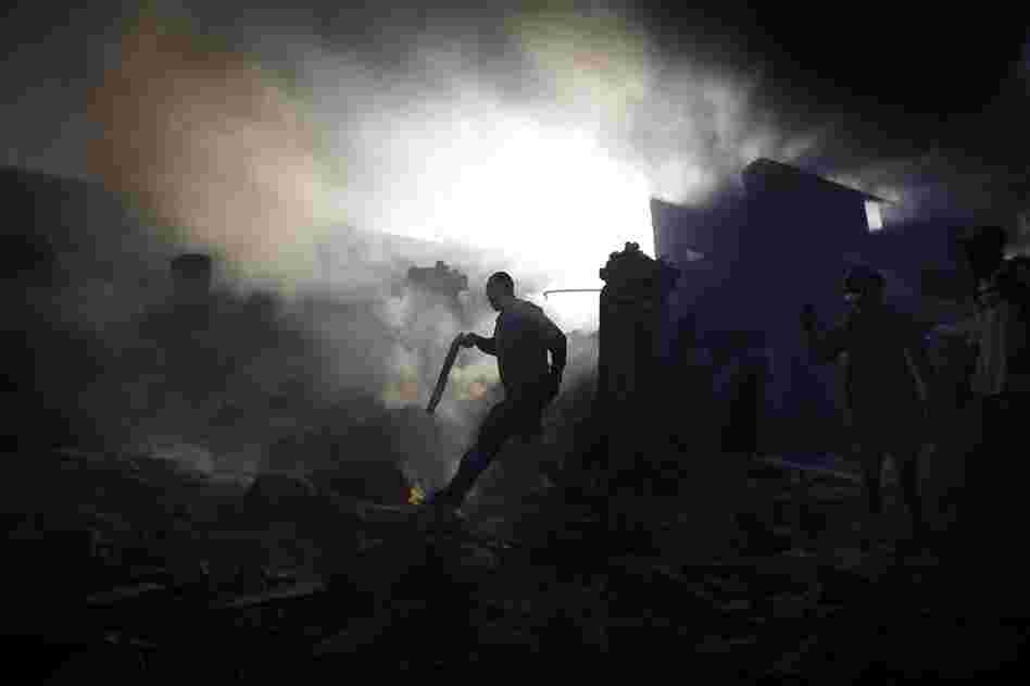 A man carries a shotgun as he walks through a collapsed burning building while trying to keep looters at bay on the streets outside in the commercial district of downtown Port-au-Prince.
