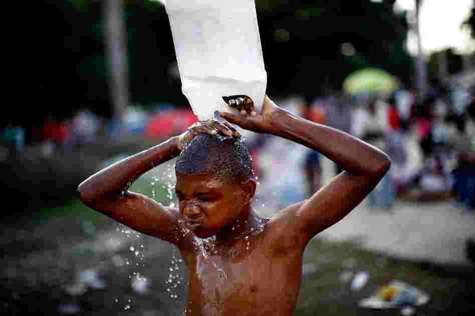 A boy uses a jug of water to wash off in a city park near the national palace.