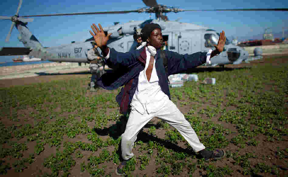 A Haitian man tries to keep a crowd from rushing a U.S. Navy helicopter as it unloads water in a Port-au-Prince park.