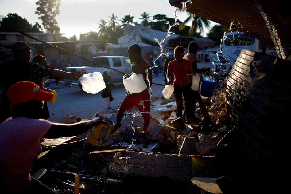 People gather around broken water pipes to collect fresh drinking water Friday in Port-au-Prince.