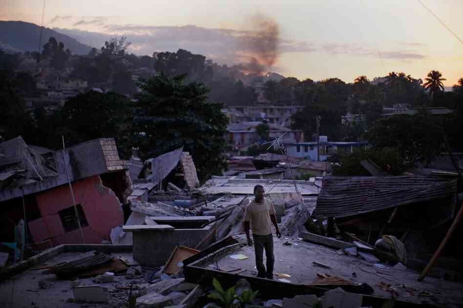 A man stands on a rooftop yelling out for any sign of his missing relatives Friday in a devastated hillside neighborhood near downtown Port-au-Prince.