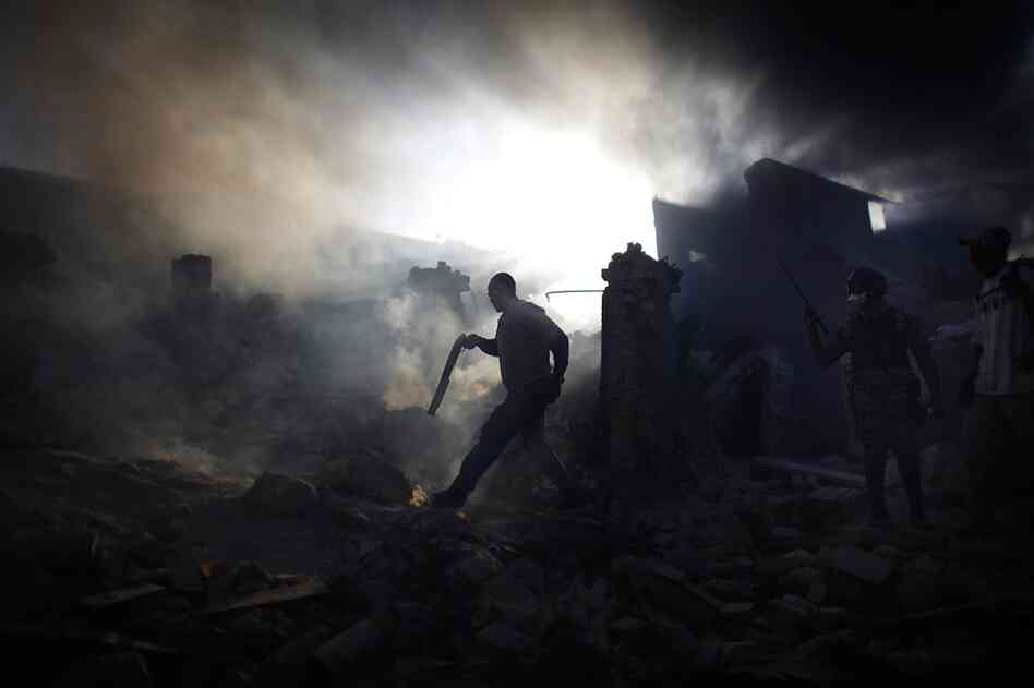 A man carries a shotgun as he walks through a collapsed burning building while trying to keep looters at bay on the streets outside in the commercial district of downtown Port-au-Prince.