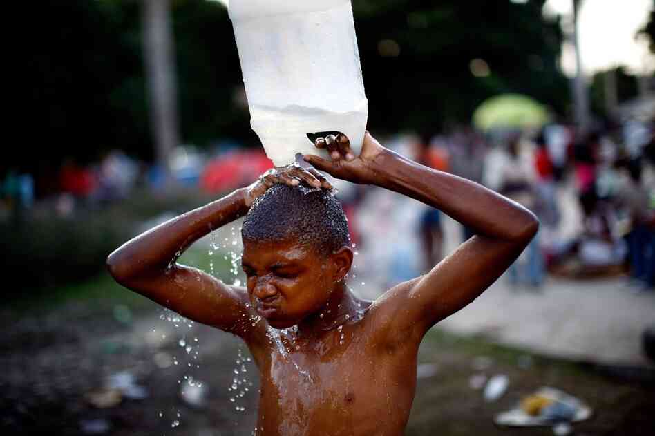 A boy uses a jug of water to wash off in a city park near the national palace.