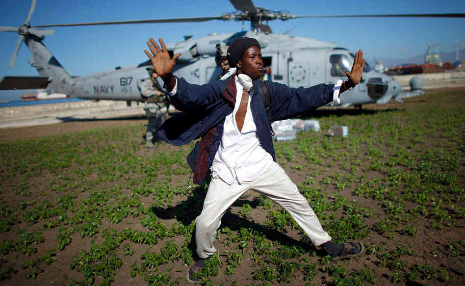 A Haitian man tries to keep a crowd from rushing a U.S. Navy helicopter as it unloads water in a Port-au-Prince park.