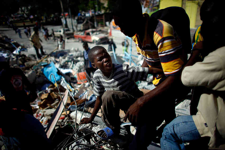 A boy tries to get a drink as looters scavenge the rubble of a supermarket Saturday in Port-au-Prince.