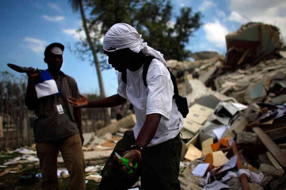 A man who has retrieved a pair of scissors from the rubble defends his actions to the guard.