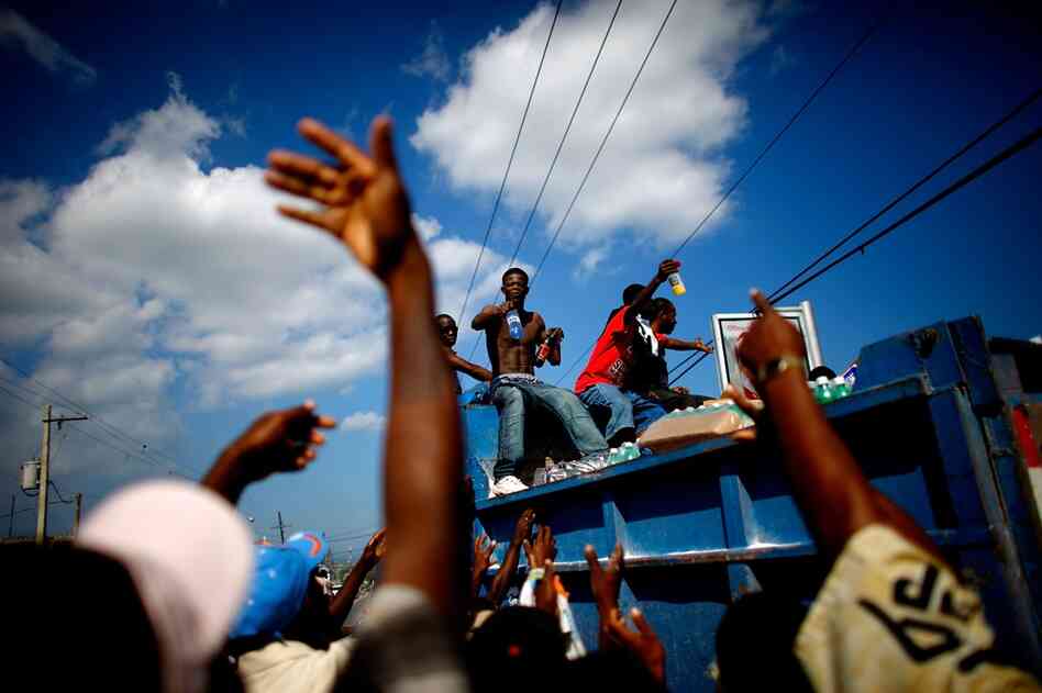 Haitian men distribute water and soda they took from a market in shambles.
