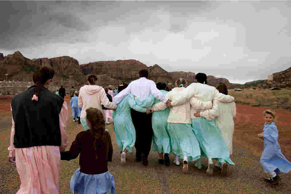 An FLDS man leaves a funeral service, linking arms with six of his wives. Only men deemed "godly" are permitted to enter into plural marriage by the church leader; those later judged unworthy can have their wives and children reassigned to other men.