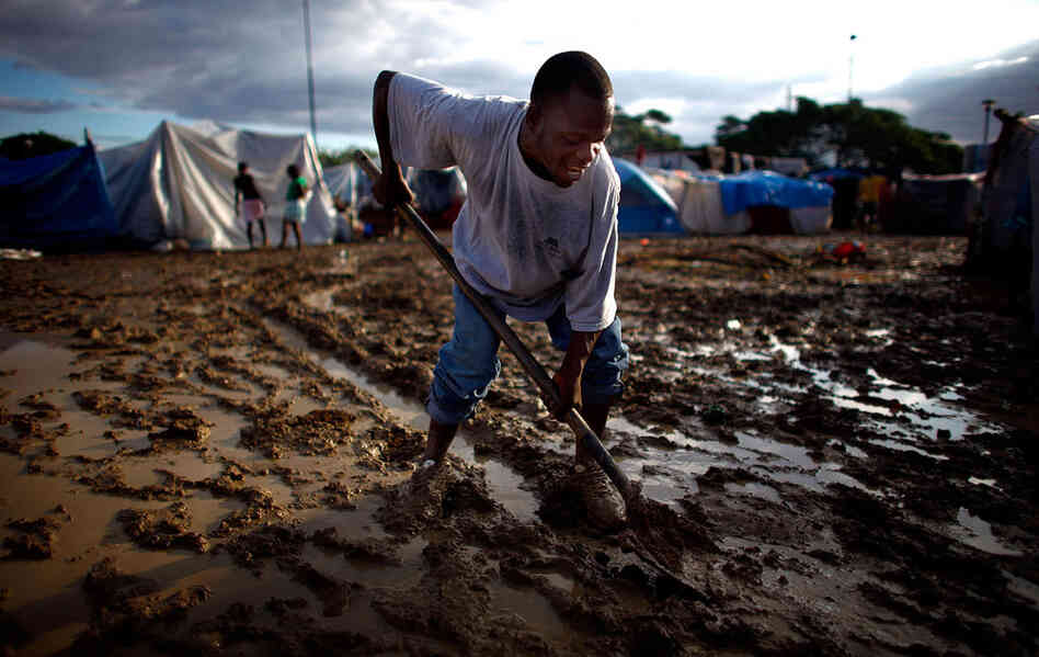 A Haitian man attempts to dig a trench in the mud to alleviate the flood damage. As the heavy rains begin, the question is no longer simply how to find housing for Haitians, but also how to keep them dry.