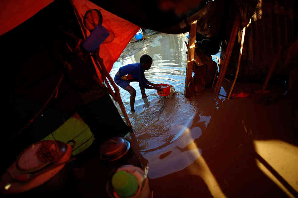 In a futile effort, Alex Mertulus scoops water with a small bucket at the entrance of his tent. His mother, Margarette, lost her husband and home in the earthquake. This is the second time she and Alex have had to move among Haiti's tent camps because of  flooding.