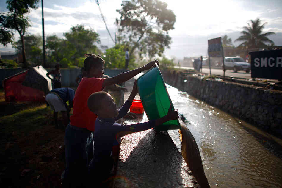 Margarette and Alex empty a bucket of dirty water into a drainage ditch.