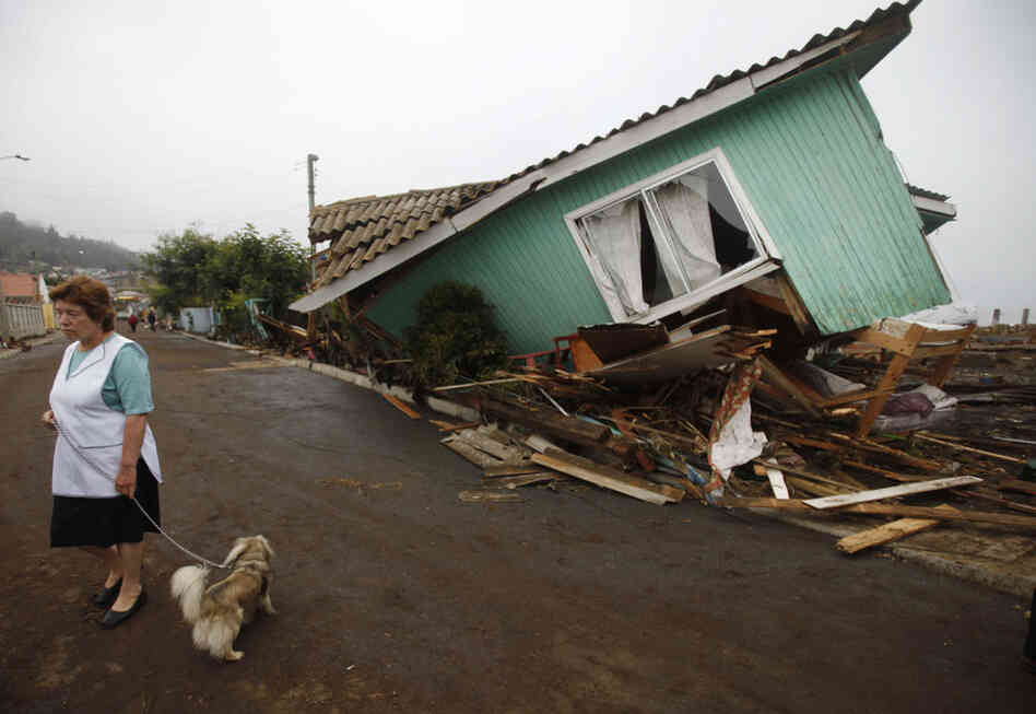 Following one of the largest earthquakes ever recorded, a woman stands in front of a destroyed home in Pelluhue.  