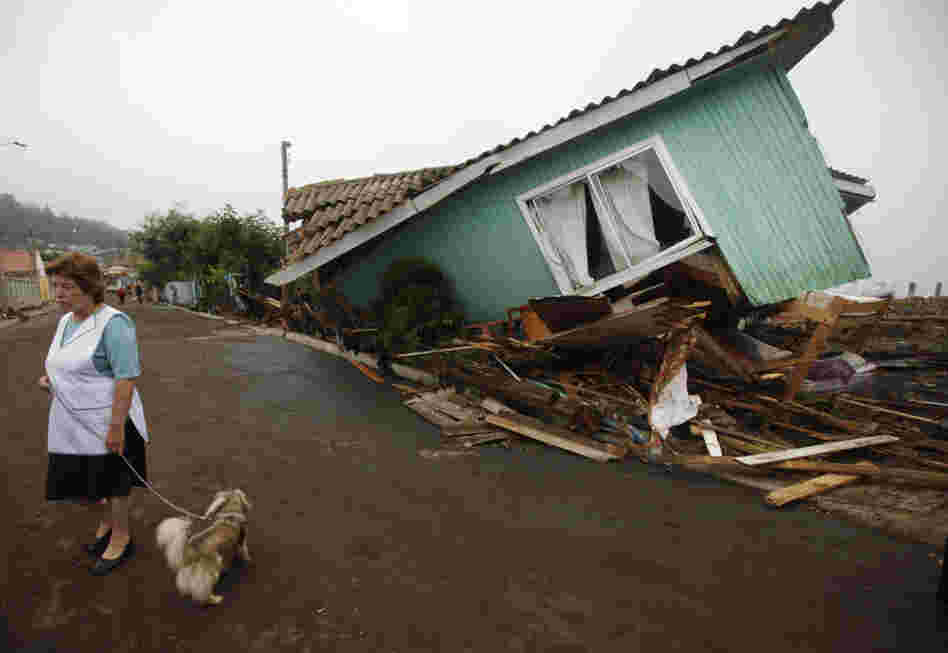 Following one of the largest earthquakes ever recorded, a woman stands in front of a destroyed home in Pelluhue.  