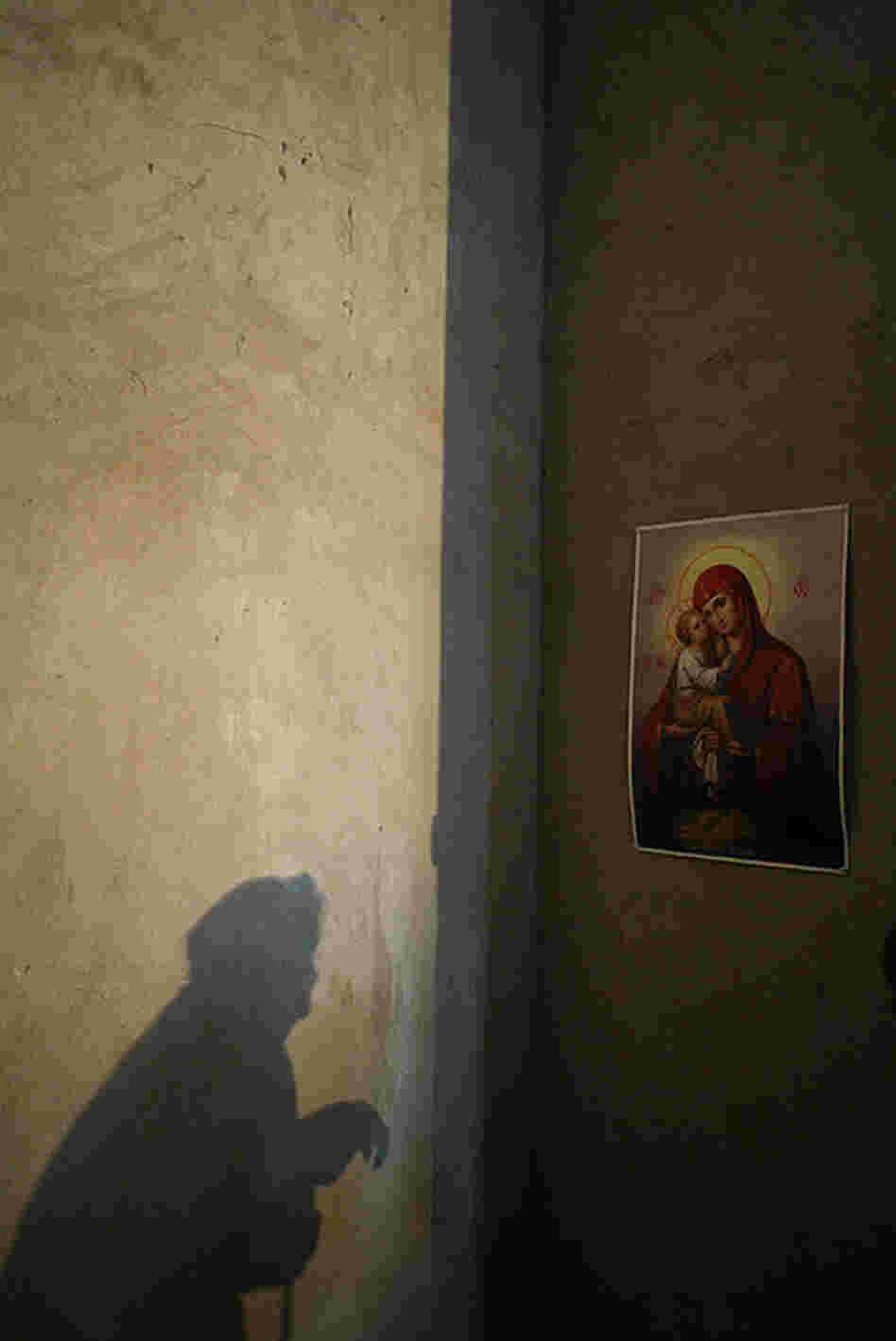 "An elderly woman prays before a poster of Mary and Jesus while Father Momotyuk Nazarii leads a service at the small Ukrainian church in Novo Ladizhichi village. The church has been under construction for a full decade, as villagers have had trouble raising enough money to continue building."