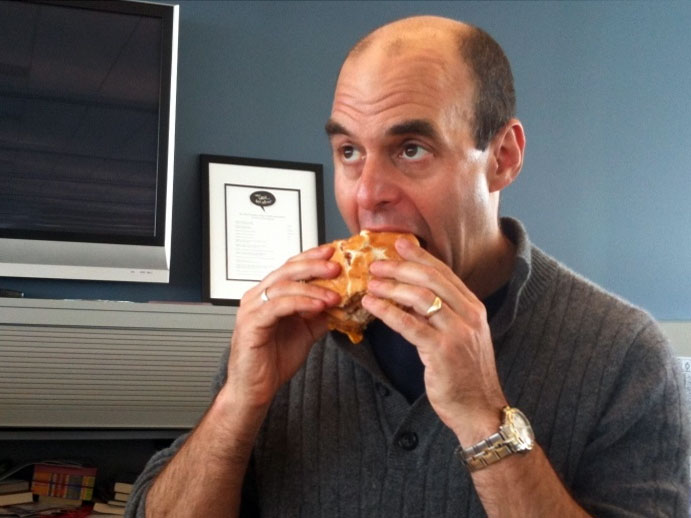 Peter Sagal bites a sandwich.