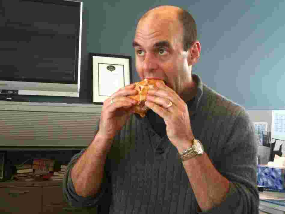Peter Sagal bites a sandwich.
