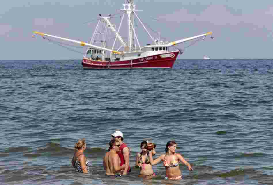 A shrimp boat skims oil from the surface of the water just off Orange Beach, Ala., as a family enjoys the surf. Oily tar balls have started washing up on Orange Beach and beaches in the western Florida panhandle. 