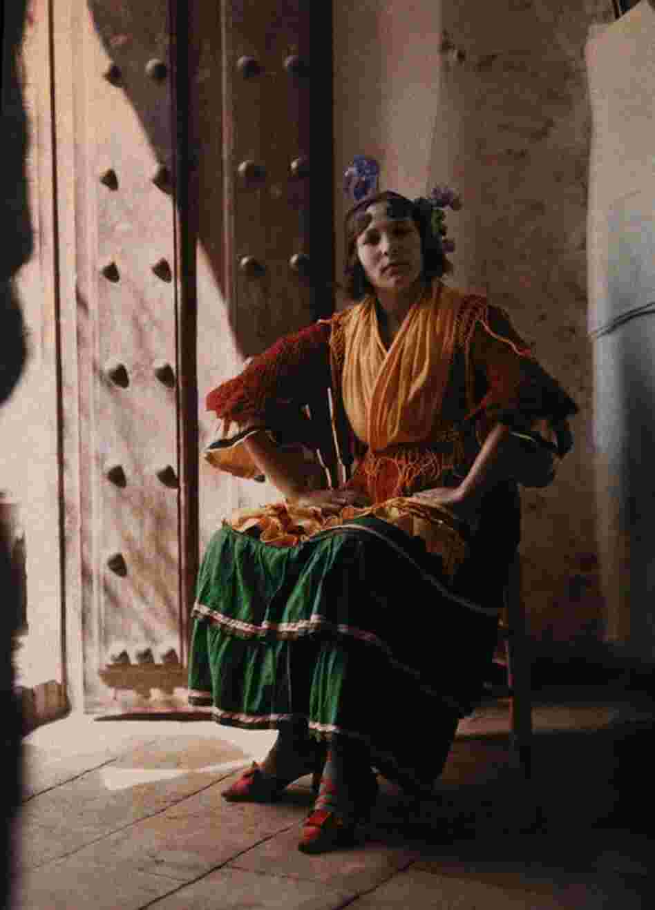 A gypsy in traditional dress poses arms akimbo in a chair, Granada, Spain, published 1929 