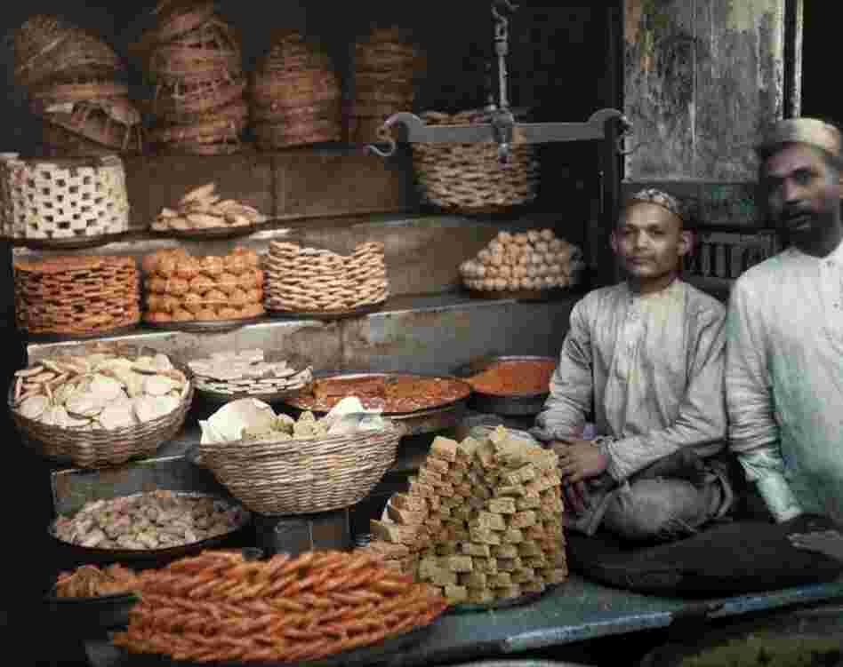 Merchants sit by their stand of honeycakes in Bombay, circa 1912 