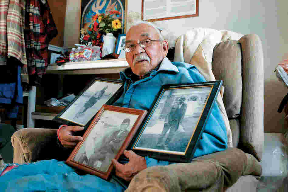 Baily Henio holds three photos. In his right hand is a photo of his warrior grandfather, Jose Pino. In the center is a photo of Henio as a young soldier during World War II. The third photo shows his father, Jake Henio.