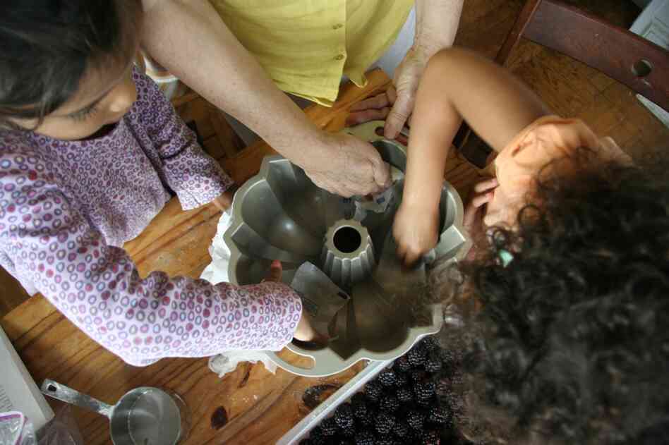 The girls grease a Bundt pan, which they will use to bake a cake with their own neighborhood ingredients.