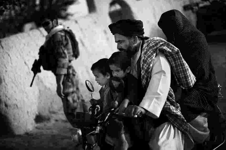 An Afghan family rides past a joint U.S.-Afghan patrol in Ezabad. Special forces aim to train communities to protect themselves. But they must first gain the trust of local Afghans, and overcome the mistrust caused by local police corruption.