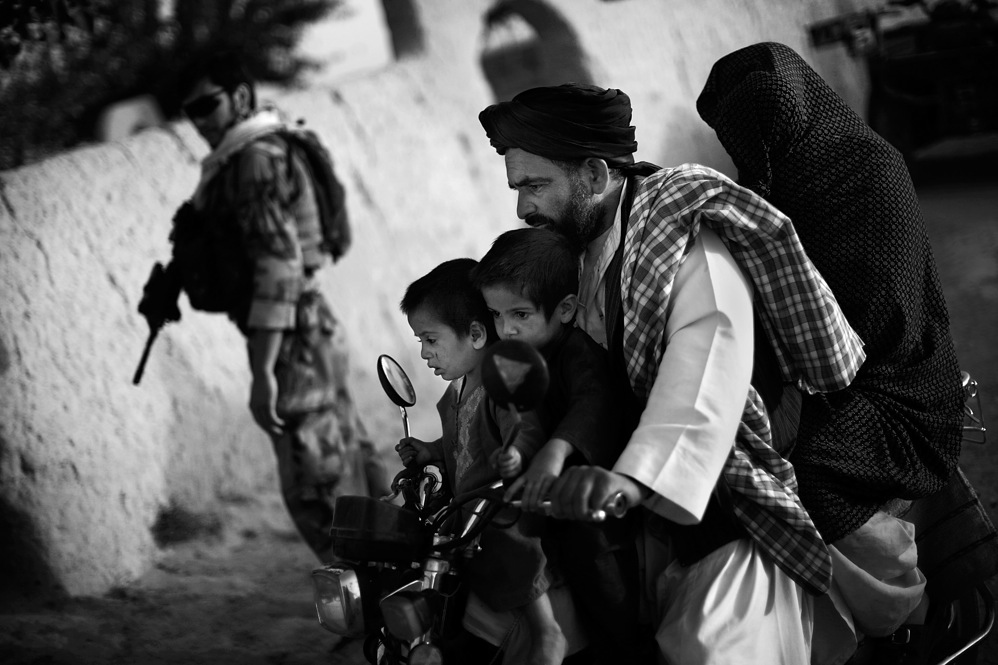 An Afghan family rides past a joint U.S.-Afghan patrol in Ezabad. Special forces aim to train communities to protect themselves. But they must first gain the trust of local Afghans, and overcome the mistrust caused by local police corruption.