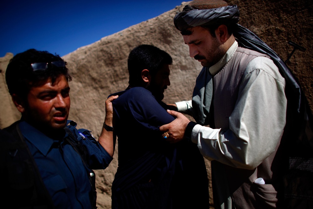 An Afghan national police officer (left) searches a man while Karim Jan (right) holds his arms. The counterinsurgency strategy relies heavily on the police, who live in the community, are closest to the people and should be able to spot insurgents.