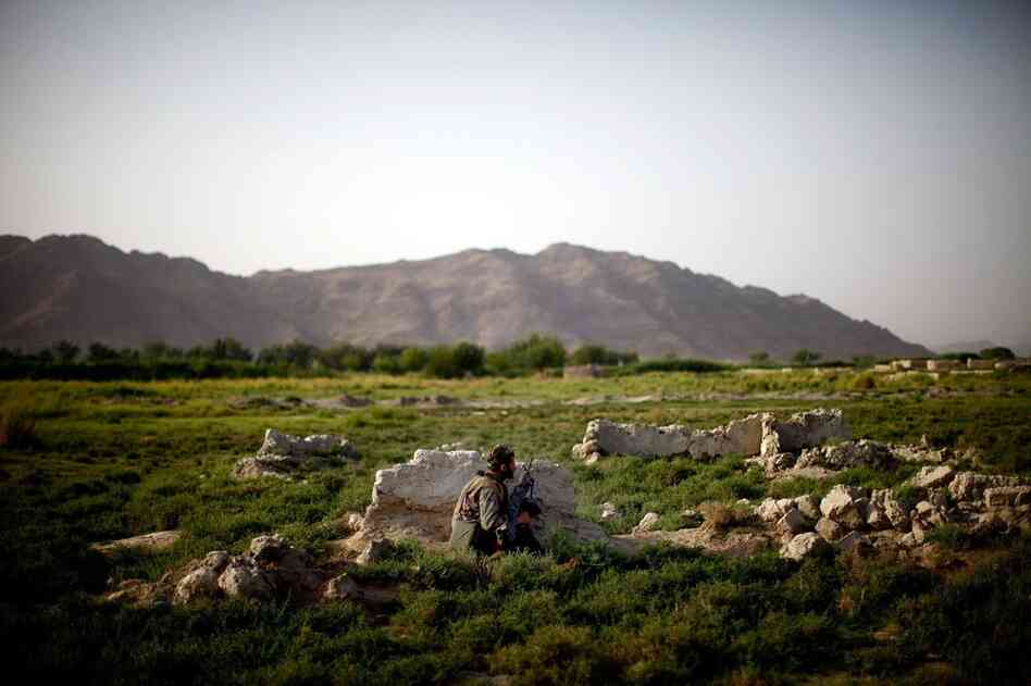An Afghan soldier on patrol with Bravo Company crouches behind a rock after gunshots are fired.